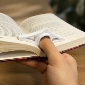 Pessoa segurando um livro aberto com uma mão usando suporte de dedo branco para leitura